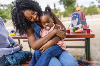 Happy african woman embracing her baby daughter in the park sitting on a picnic table
