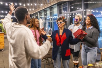 Multiracial friends celebrating surprise birthday party for a woman at night in the terrace of a