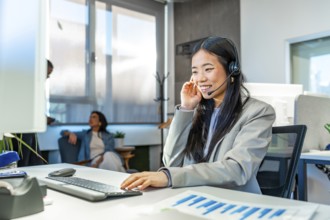 Young asian manager wearing headset working with computer in a coworking office, colleagues talking