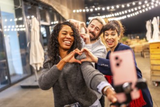 Multi-ethnic friends join hands gesturing heart shape while vlogging online in a night party