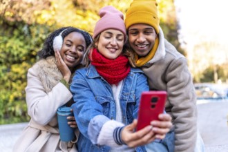 Multiracial young friends having fun together taking a selfie with smartphone in a winter city