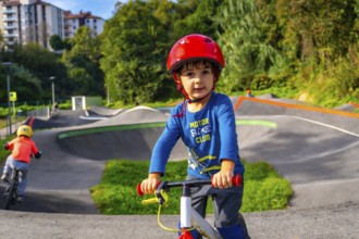 A young boy in a blue shirt and helmet is riding a bike on a dirt track. The boy is smiling and he
