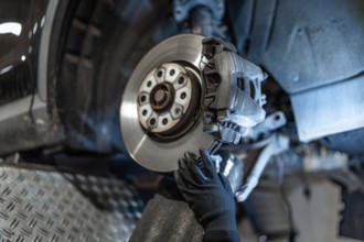 Close up of mechanic's hands wearing gloves, inspecting car brake disc and caliper during