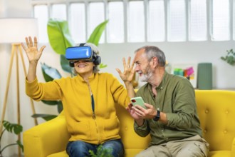Mature couple having fun together wearing virtual reality glasses and mobile phone sitting on the