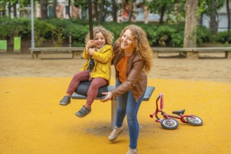 Caucasian adult mother pushing a girl on a swing in a park