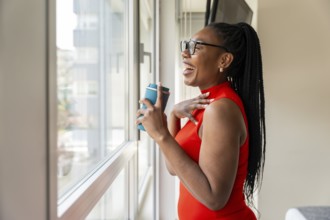 Happy businesswoman laughing while holding a reusable coffee cup and looking out the window of her