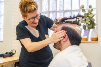 Hairdresser attaching a new capillary prosthesis to a man using adhesive stripes