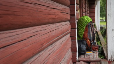 A pilgrim's rucksack standing against a wooden shed painted falun red, medieval church, pole,