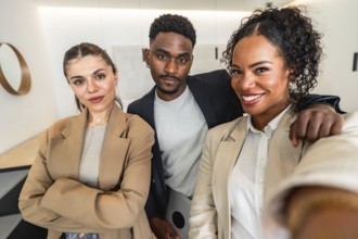 Three smiling businesspeople are taking a selfie in a modern office, showing teamwork and