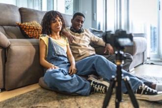 Two content creators recording a video blog in their living room using a camera on tripod