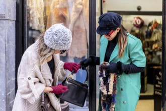 Young blonde girl shopping in the city and served by a shop assistant, looking at shop windows of