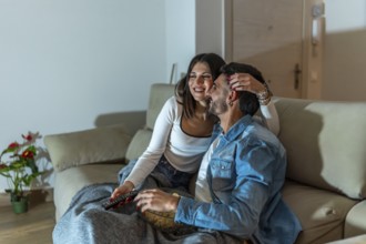 Young loving couple watching television, eating popcorn and relaxing on sofa at night at home