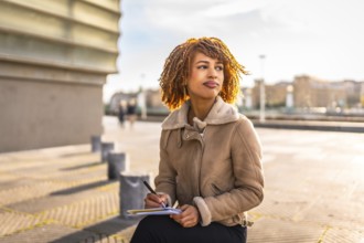 Beauty latin woman with curly hair writing notes sitting in the city during a cold and sunny day