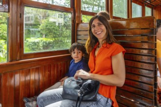 A woman and a child are sitting on a train. The woman is smiling and holding a purse