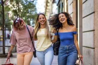 Happy diverse female friends walking embraced enjoying a day shopping at city