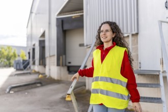 Woman worker in yellow reflective clothes walking out a distribution warehouse
