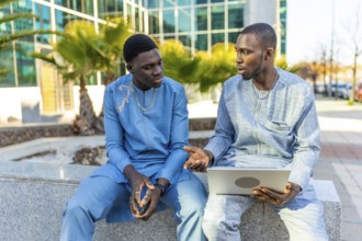 Two senegalese businessmen wearing traditional dashiki attire are sitting outside a modern office