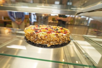 An artistically decorated cake with almond slivers and fruit in a glass display case, Cafe Kuh,