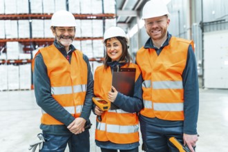 Warehouse workers wearing safety vests and hard hats smiling in a logistics center, managing