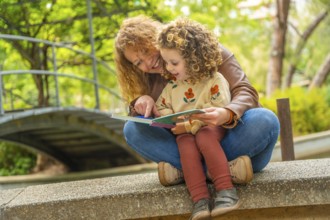Girl sitting on the lap of her mother reading a book in a park