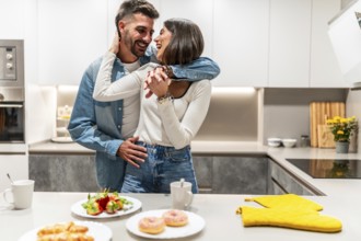 Young couple hugging and laughing in their modern kitchen, enjoying a romantic moment together with