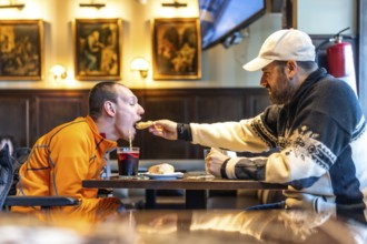 Heartwarming moment of friendship as a man helps his disabled friend enjoy a meal at a restaurant,