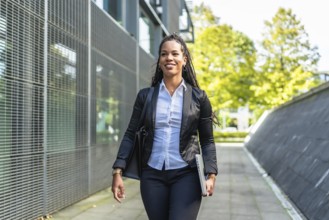 Real estate agent latin woman walking outside building holding laptop