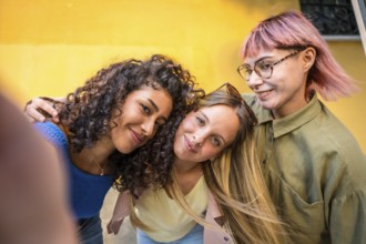 Three casual diverse young woman taking selfie against yellow wall
