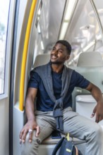Vertical photo of a happy african entrepreneur sitting on the metro looking through window