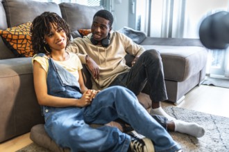 Young black couple relaxing on floor and sofa in living room, holding hands and enjoying time
