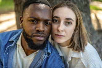 Close-up frontal view of a multiracial couple together cheek to cheek in a park