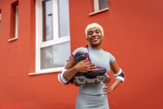 Portrait of african female skater with inline skates on shoulder standing outdoors next to red