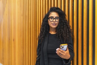 Portrait of an young adult latin businesswoman in black elegant clothes using mobile phone indoors
