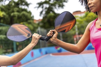 Cropped close-up photo of multiracial women clashing pickelball rackets before playing together