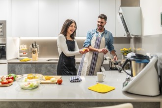 Cheerful couple wearing aprons preparing healthy meal together, having fun in contemporary kitchen