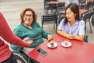 Woman with disability and asian friend paying with credit card in a sidewalk cafeteria