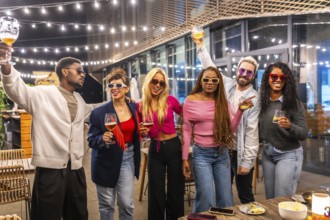 Multi-ethnic friends raising glasses celebrating party at night in the terrace of a modern bar