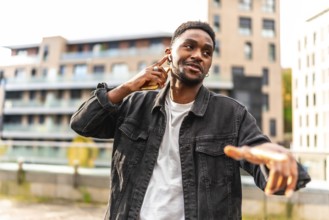 African cool man listening to music with earbuds and dancing in the city street