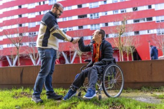 Two friends shaking hands in a city park, one of whom is using a wheelchair, demonstrating support