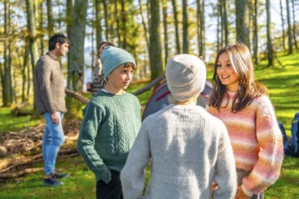 Caucasian sister and brothers talking standing in a green forest while camping with their parents