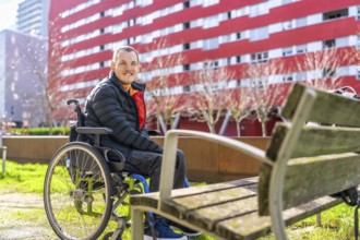 Portrait of a cheerful young disabled man sitting in a wheelchair enjoying a sunny day in a city