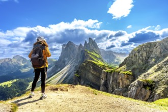 Female tourist with backpack admiring the odle mountain range in the italian dolomites on a sunny