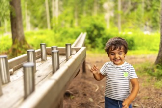Young boy having fun interacting with a wooden sensory play table with metal cylinders in a natural