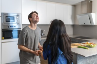 Asian woman and caucasian man sharing a joyful moment in a bright, contemporary kitchen,