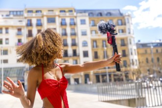 Female latin young vlogger recording a video in the city using mobile phone and microphone