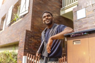 Confident african entrepreneur leaning on a house entrance holding laptop