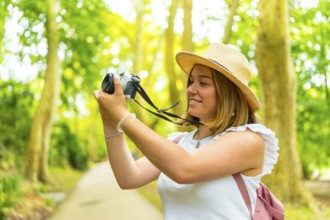 Close up side view of a caucasian young cheerful woman hiking in the forest with camera