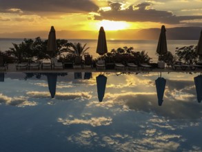 Sunset illuminated Red Sea and clouds Altostratus closed parasols reflected in swimming pool,