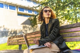 Modern arab businesswoman using laptop sitting on park bench working on remote