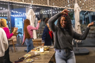 Latin woman dancing happily while partying with diverse friends in a roof bar at night